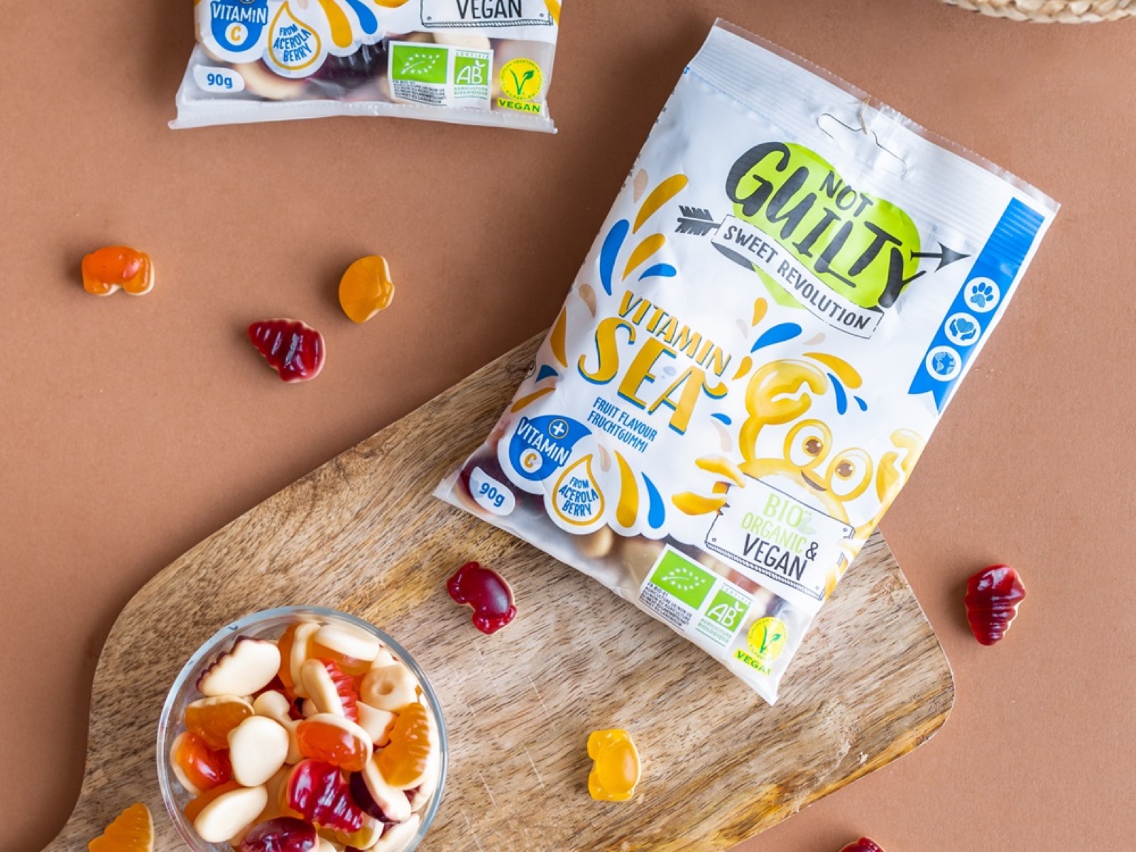 Zwei Tüten veganes Fruchtgummi von Not Guilty neben einer Glasschale mit Fruchtgummis auf einem Holzbrett