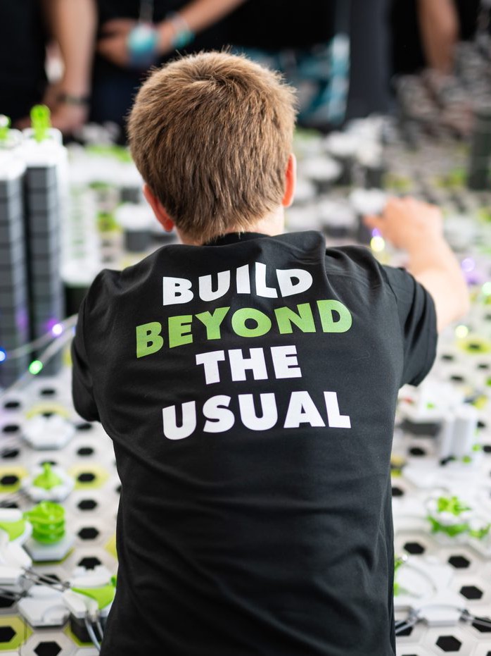 Teilnehmer im Event-Shirt „Build beyond the usual“ baut an der großen Gravitrax-Kugelbahn